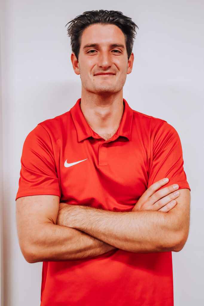 torso and head shot. arms crossed wearing a red polo smiling at the camera